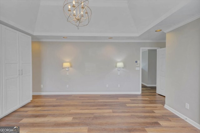 spare room with light wood-type flooring, a tray ceiling, an inviting chandelier, and crown molding