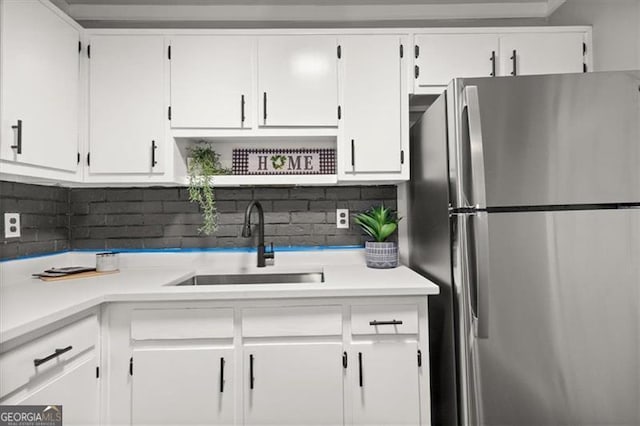 kitchen with backsplash, stainless steel fridge, white cabinetry, and sink