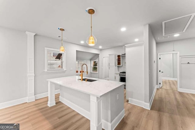 kitchen with sink, decorative light fixtures, light hardwood / wood-style flooring, white cabinets, and an island with sink