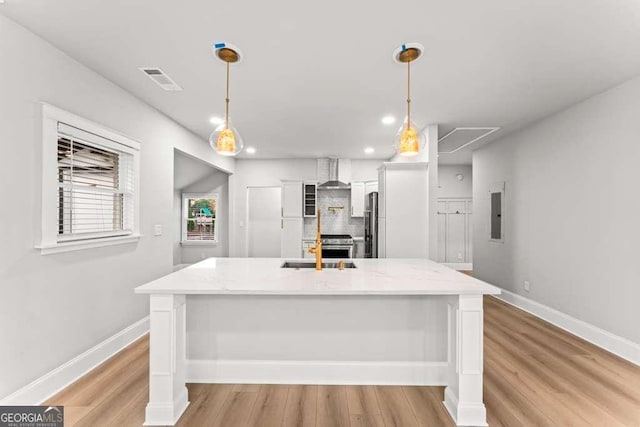 kitchen with white cabinets, decorative light fixtures, wall chimney exhaust hood, and light hardwood / wood-style floors