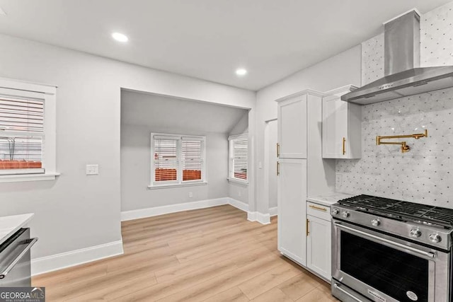 kitchen with appliances with stainless steel finishes, white cabinetry, a healthy amount of sunlight, and wall chimney range hood