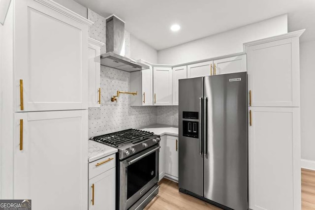 kitchen featuring light hardwood / wood-style floors, wall chimney range hood, stainless steel appliances, and white cabinetry