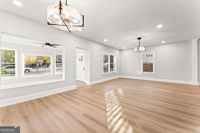 unfurnished living room with ceiling fan with notable chandelier and light wood-type flooring