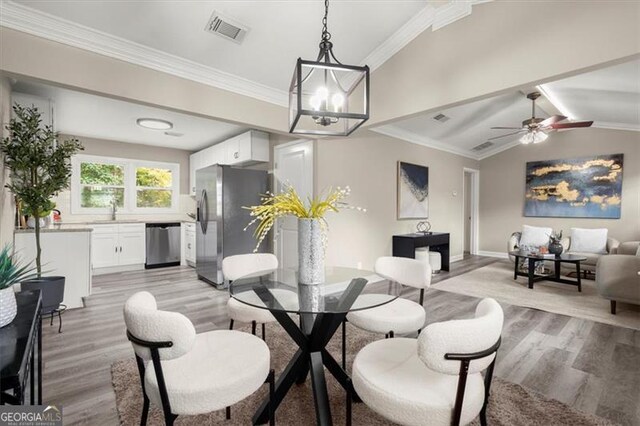 dining space featuring light hardwood / wood-style floors, vaulted ceiling, ornamental molding, and sink