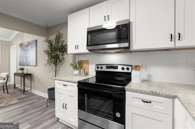 kitchen with light stone countertops, light hardwood / wood-style flooring, appliances with stainless steel finishes, white cabinets, and ornamental molding