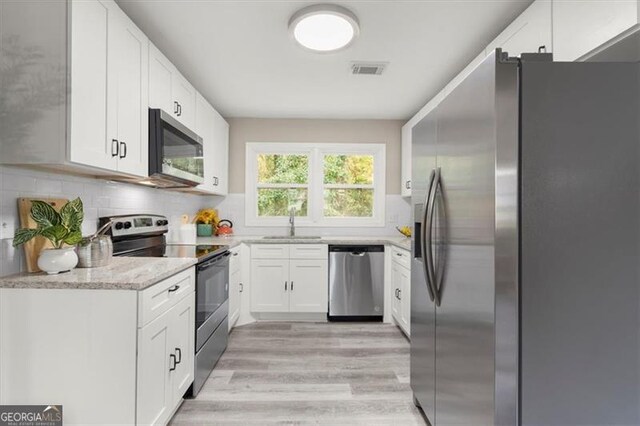 kitchen with light stone countertops, white cabinetry, sink, stainless steel appliances, and light hardwood / wood-style floors