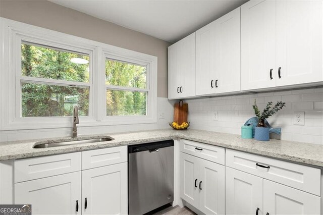 kitchen with light stone countertops, tasteful backsplash, stainless steel dishwasher, sink, and white cabinetry