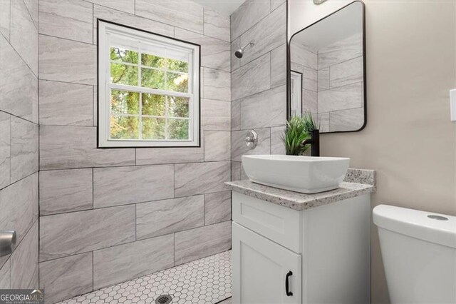 bathroom featuring a tile shower, vanity, and toilet