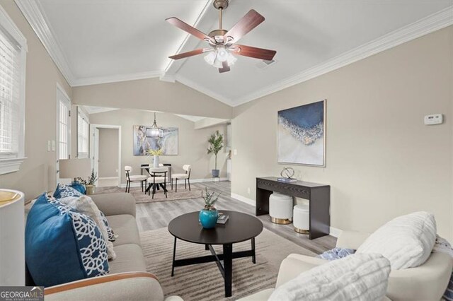 living room featuring vaulted ceiling with beams, light wood-type flooring, ceiling fan with notable chandelier, and ornamental molding