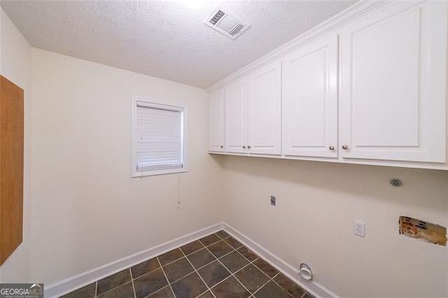 clothes washing area with hookup for an electric dryer, cabinets, dark tile patterned floors, and a textured ceiling