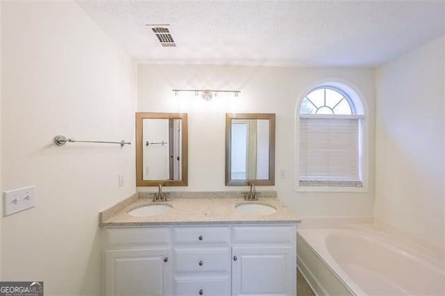 bathroom with a tub, vanity, and a textured ceiling