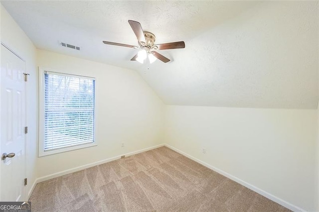 additional living space featuring a textured ceiling, ceiling fan, light colored carpet, and vaulted ceiling