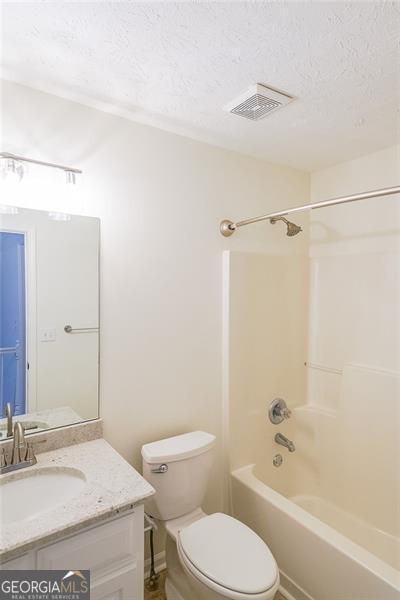 full bathroom with vanity, shower / bathing tub combination, a textured ceiling, and toilet