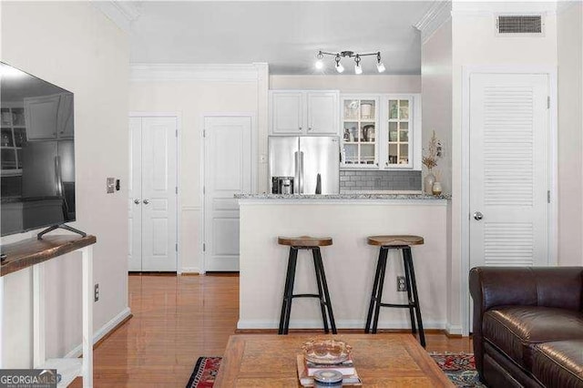 kitchen with white cabinetry, light stone countertops, stainless steel refrigerator with ice dispenser, decorative backsplash, and ornamental molding