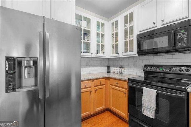 kitchen with light stone countertops, decorative backsplash, black appliances, light hardwood / wood-style flooring, and white cabinetry