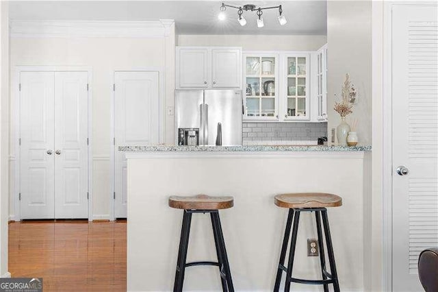 kitchen featuring white cabinets, decorative backsplash, stainless steel fridge, light stone countertops, and a breakfast bar area