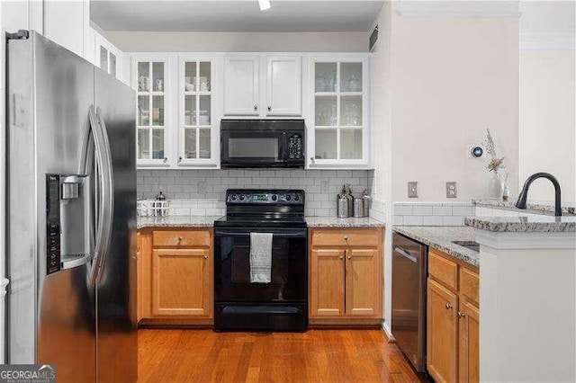 kitchen featuring black appliances, white cabinetry, light wood-type flooring, and light stone countertops