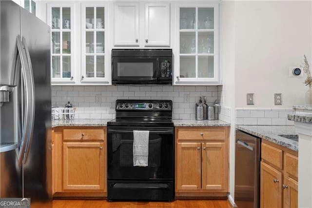 kitchen featuring backsplash, black appliances, light hardwood / wood-style floors, light stone counters, and white cabinetry