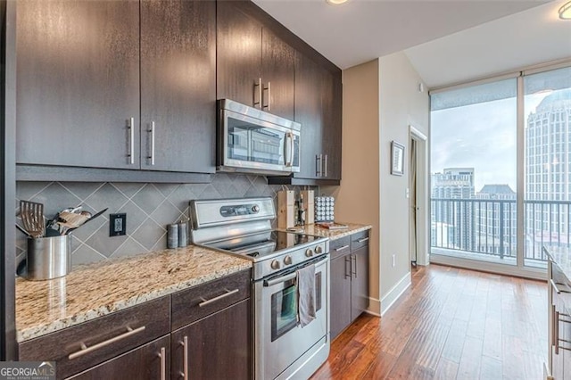 kitchen featuring decorative backsplash, light stone countertops, appliances with stainless steel finishes, dark brown cabinets, and dark hardwood / wood-style flooring