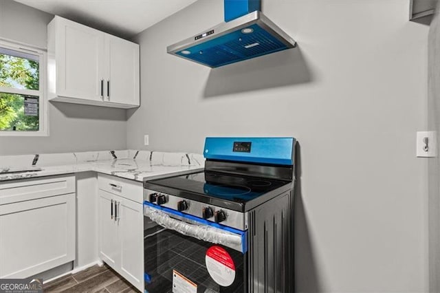 kitchen featuring stainless steel electric range oven, light stone countertops, wall chimney range hood, and white cabinetry