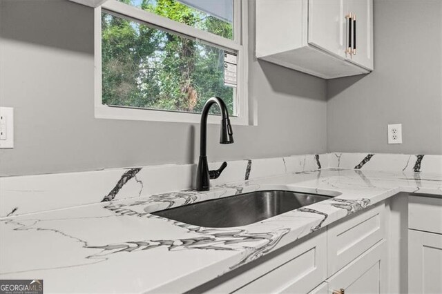 kitchen featuring white cabinets, light stone countertops, a wealth of natural light, and sink