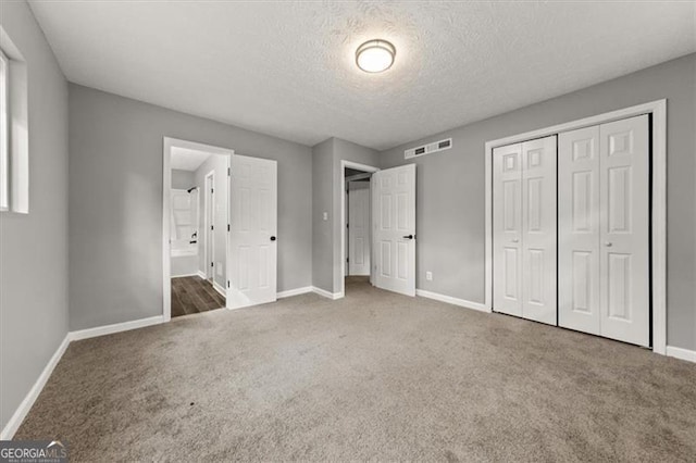 unfurnished bedroom with a textured ceiling, connected bathroom, a closet, and dark colored carpet