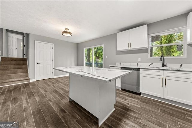 kitchen featuring light stone countertops, stainless steel dishwasher, a kitchen island, white cabinets, and sink