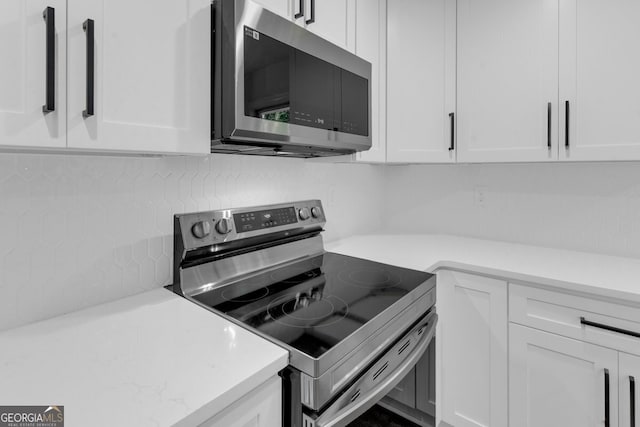 kitchen featuring white cabinets, appliances with stainless steel finishes, tasteful backsplash, and light stone counters