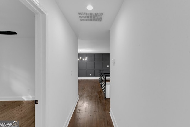 corridor with dark hardwood / wood-style flooring and an inviting chandelier