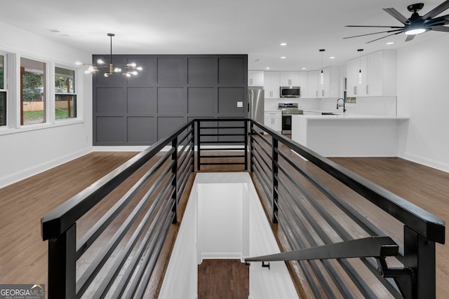 stairway with wood-type flooring, ceiling fan with notable chandelier, and sink