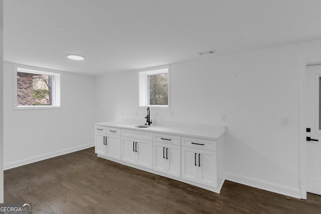 bar featuring dark hardwood / wood-style flooring, white cabinetry, and sink