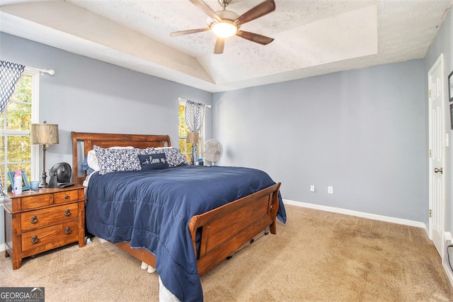 carpeted bedroom with a tray ceiling, a textured ceiling, baseboards, ceiling fan, and vaulted ceiling