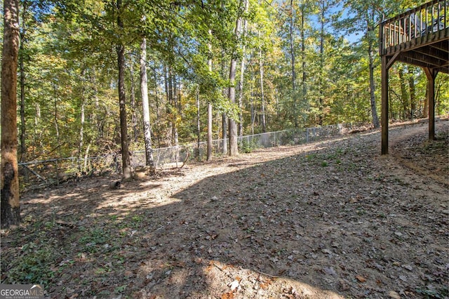 view of yard featuring a wooden deck, a view of trees, and fence