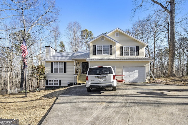 split level home with metal roof, a garage, driveway, and a chimney