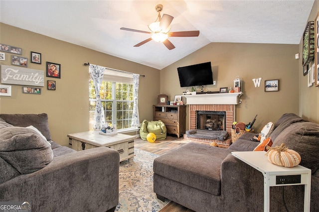 living area with a ceiling fan, lofted ceiling, a brick fireplace, and wood finished floors