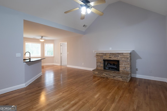 unfurnished living room with ceiling fan, sink, high vaulted ceiling, hardwood / wood-style floors, and a stone fireplace