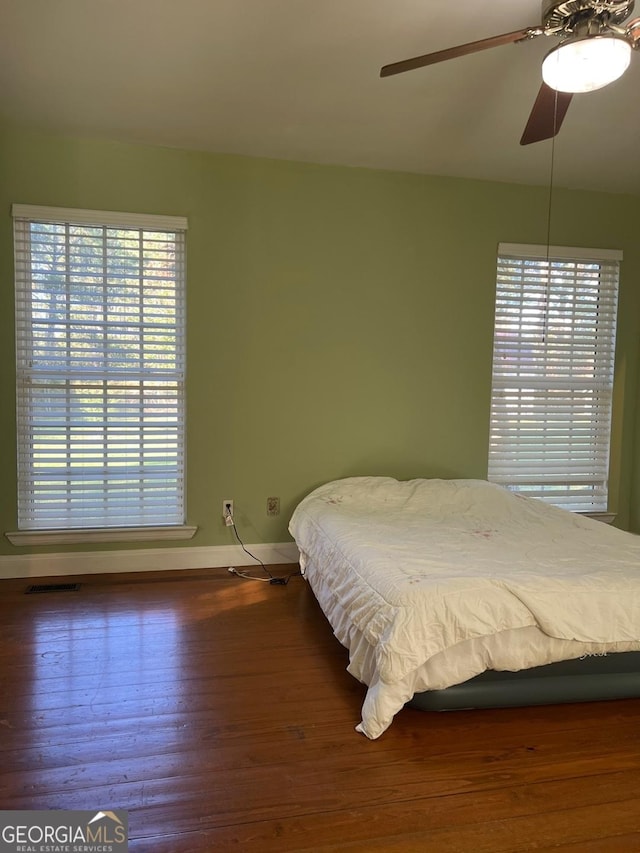 bedroom featuring ceiling fan, dark hardwood / wood-style flooring, and multiple windows