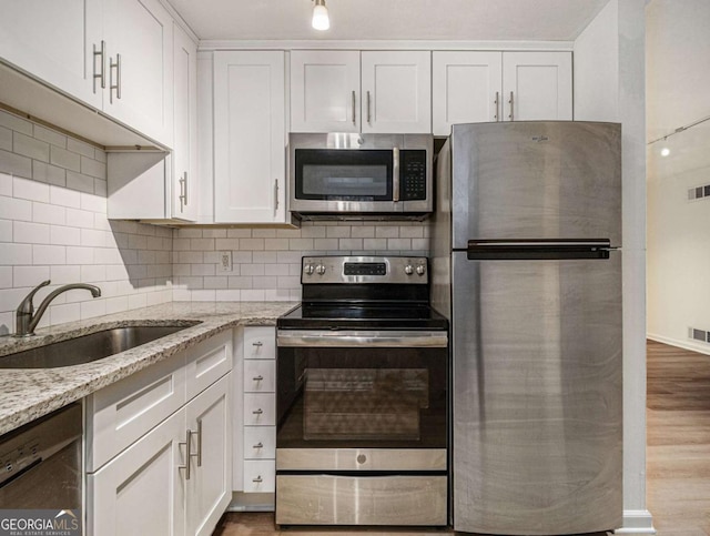 kitchen with light stone countertops, appliances with stainless steel finishes, sink, hardwood / wood-style flooring, and white cabinetry