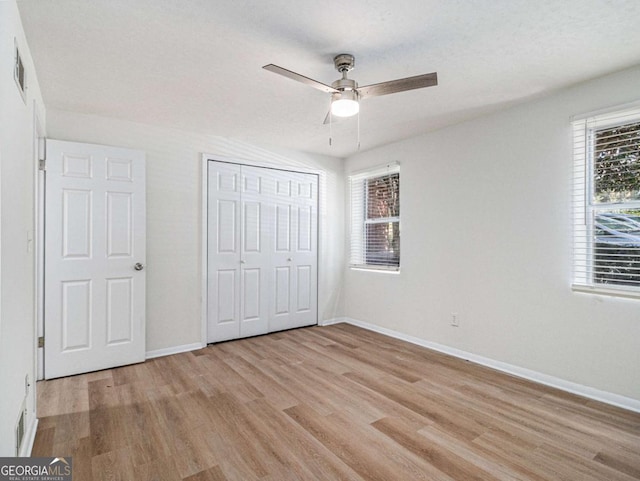 unfurnished bedroom featuring multiple windows, ceiling fan, a closet, and light wood-type flooring