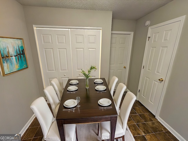 dining space featuring dark tile patterned flooring, baseboards, and a textured ceiling