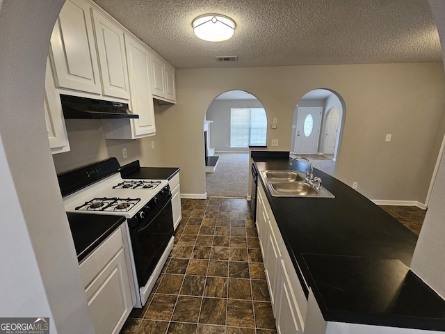 kitchen with visible vents, under cabinet range hood, a sink, dark countertops, and gas stove