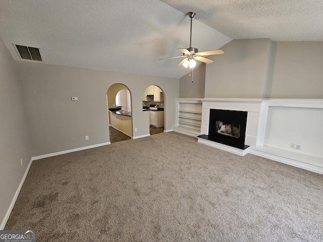 unfurnished living room featuring visible vents, a fireplace with raised hearth, dark carpet, arched walkways, and vaulted ceiling