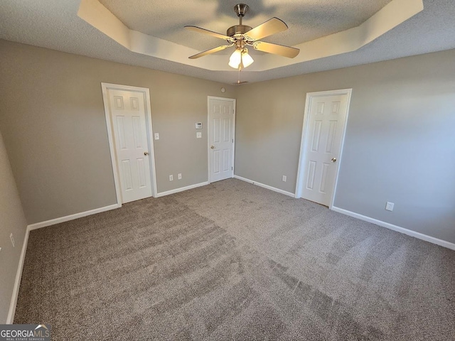 unfurnished bedroom with baseboards, carpet flooring, a textured ceiling, and a tray ceiling