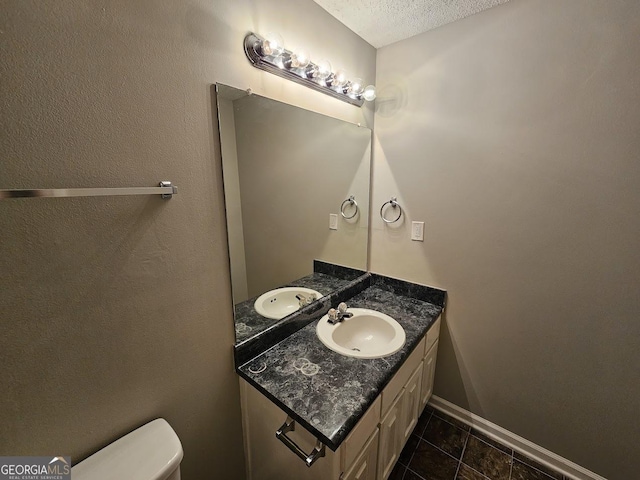 half bathroom with baseboards, toilet, vanity, and a textured ceiling