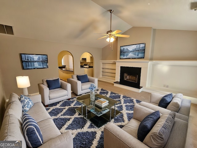 carpeted living area featuring ceiling fan, visible vents, a fireplace with raised hearth, and vaulted ceiling