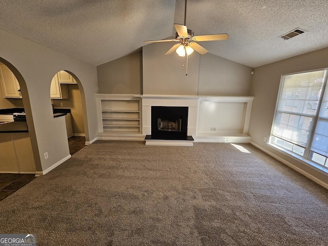 unfurnished living room featuring visible vents, a fireplace with raised hearth, baseboards, dark colored carpet, and lofted ceiling