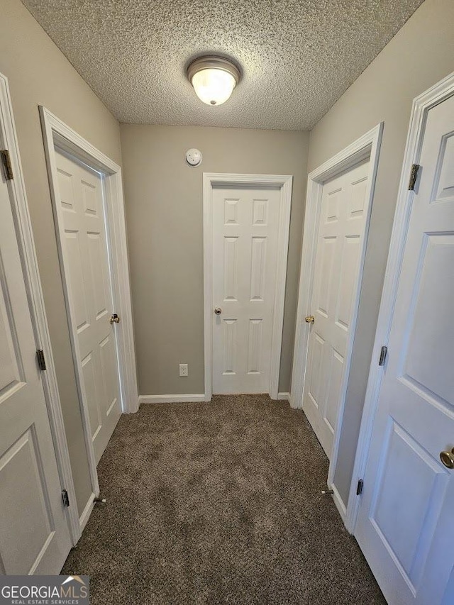 hall with baseboards, dark colored carpet, and a textured ceiling