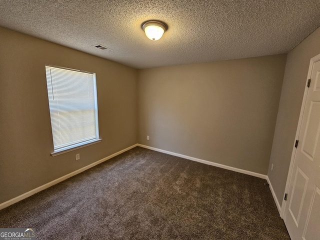 spare room featuring visible vents, dark carpet, a textured ceiling, and baseboards