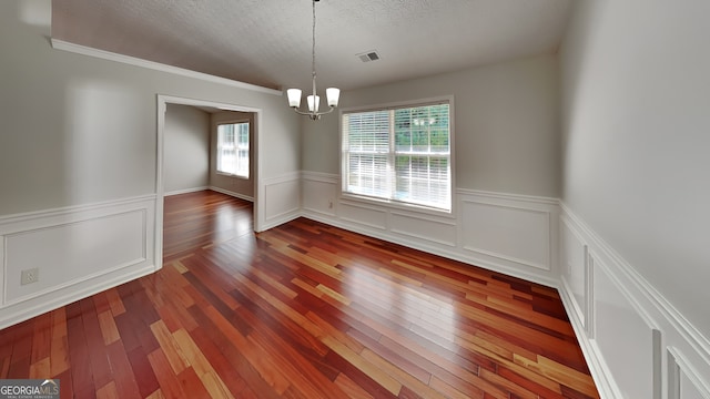 unfurnished dining area featuring hardwood / wood-style floors, a textured ceiling, a wealth of natural light, and a notable chandelier