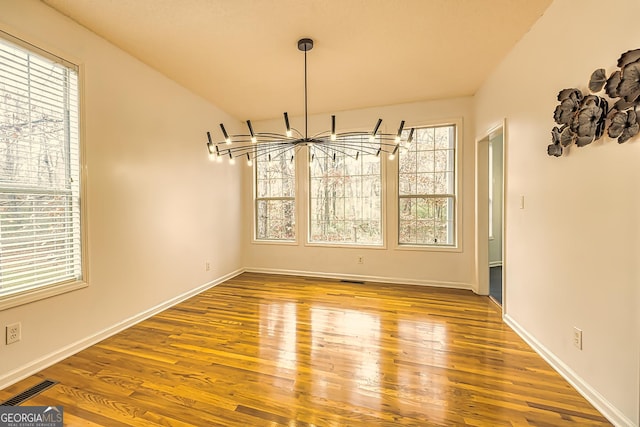 unfurnished dining area with wood-type flooring and an inviting chandelier